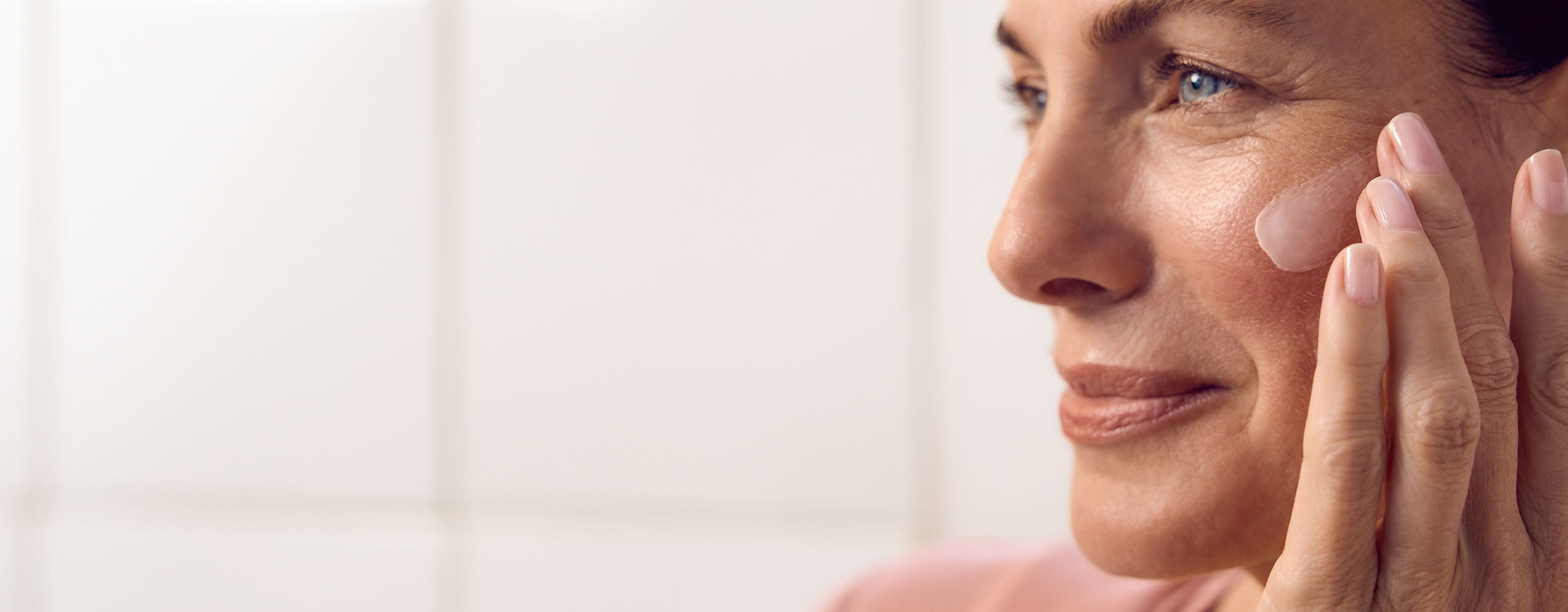 Vue d'une personne qui s'enduit le visage d'une crème NIVEA tout en souriant et en regardant au loin.