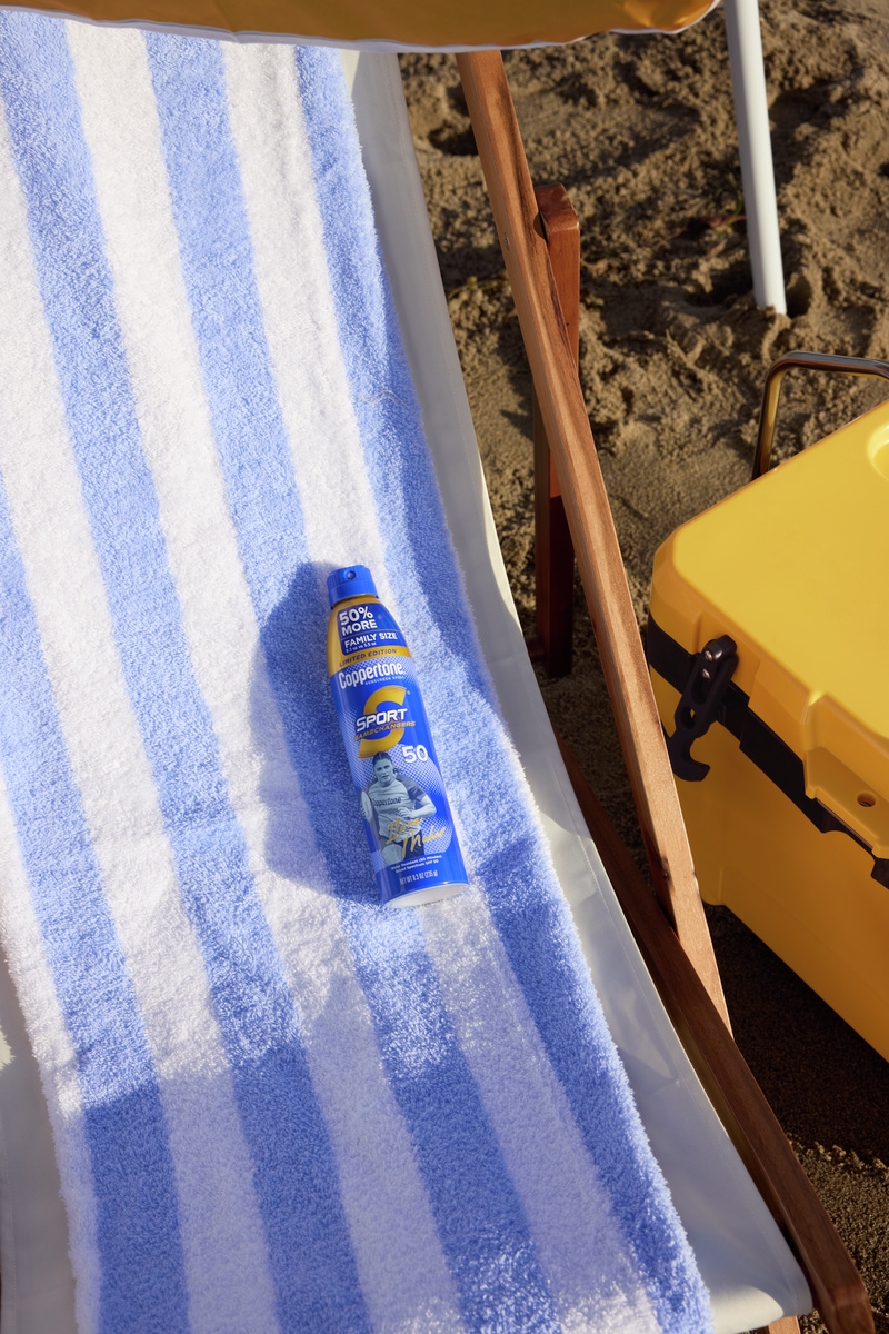 Coppertone Sport sunscreen spray bottle on a blue striped beach towel