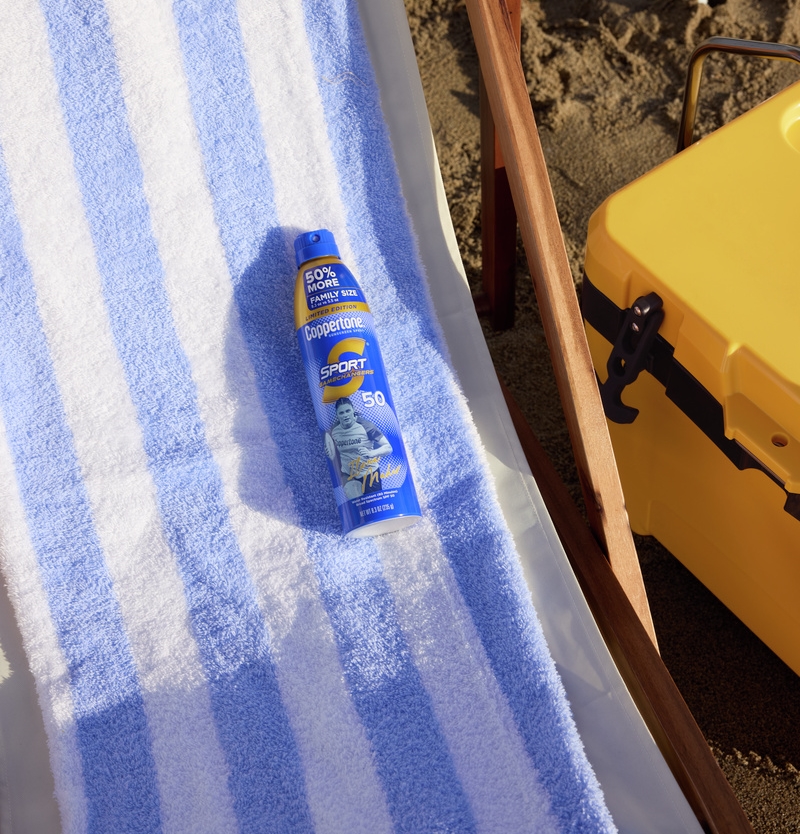 Coppertone Sport sunscreen spray bottle on a blue striped beach towel