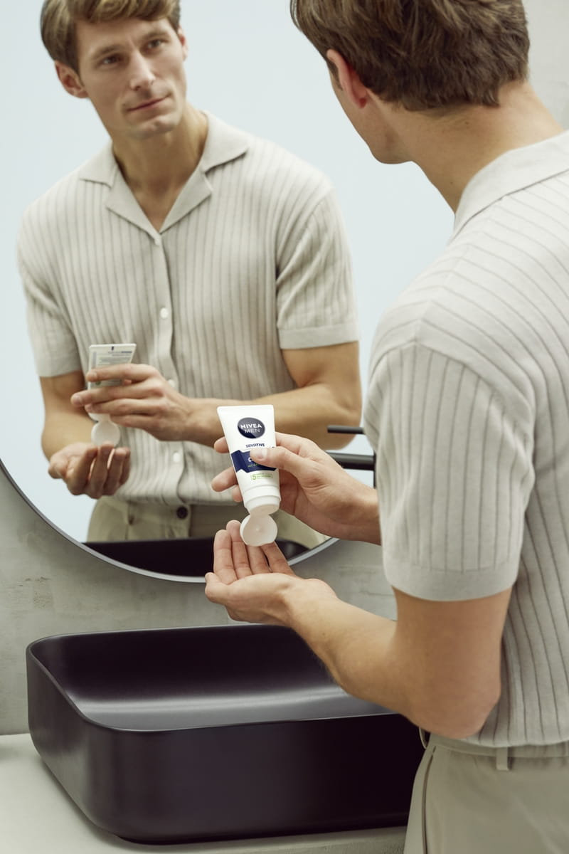 blonde man with a stubble in a white t-shirt standing in the bathroom