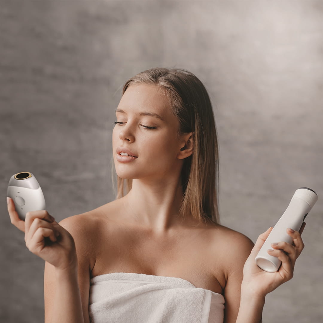 Woman in towel holding two skincare devices.