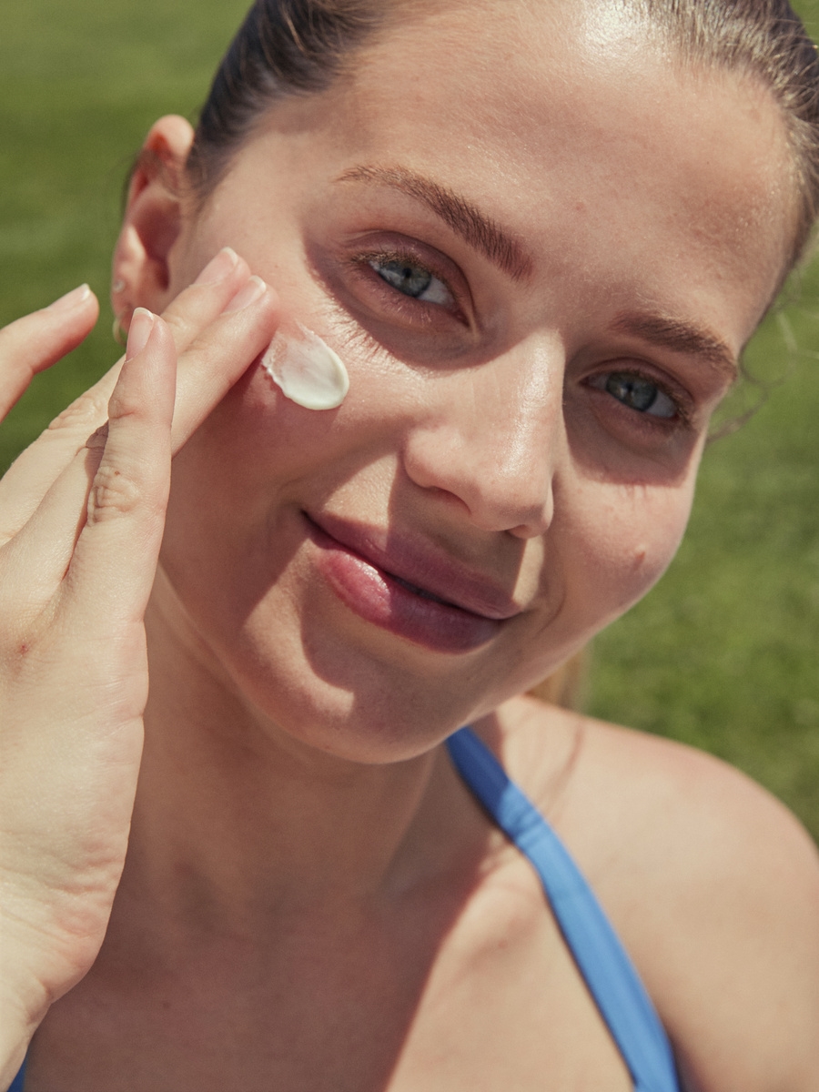 Close-up of a woman applying facial sunscreen cream to her cheek outdoors