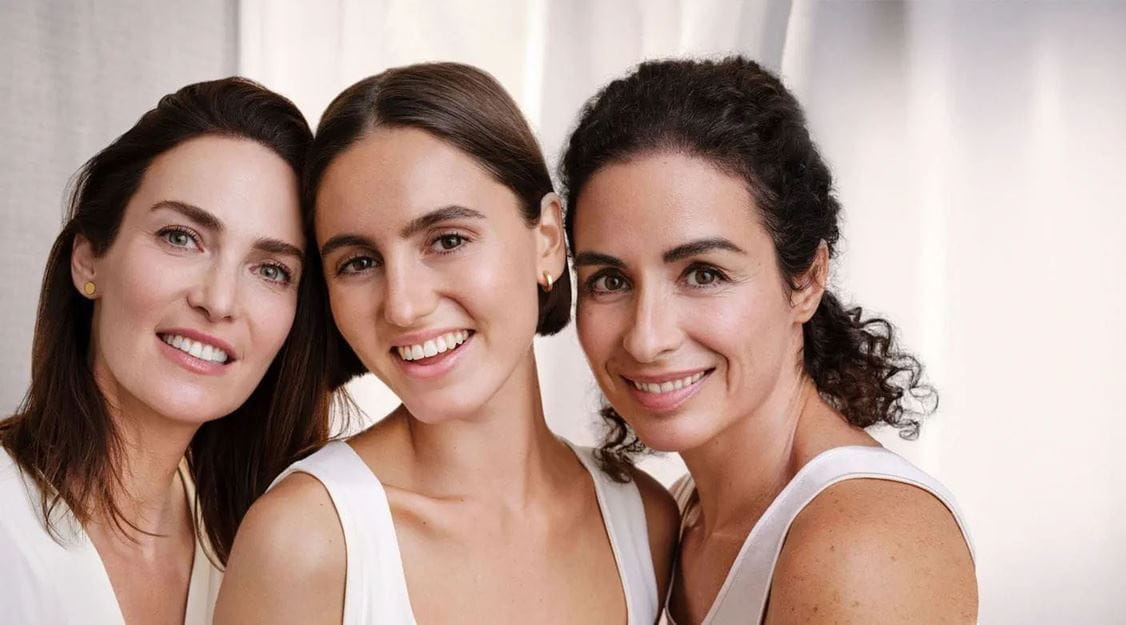 Three middle-aged women smiling with reduced face wrinkles, dark spots, and age spots.