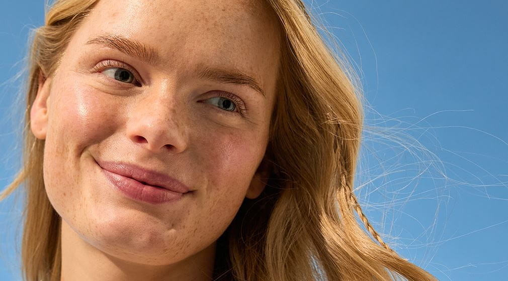 Blonde vrouw raakt haar huid aan en kijkt in camera