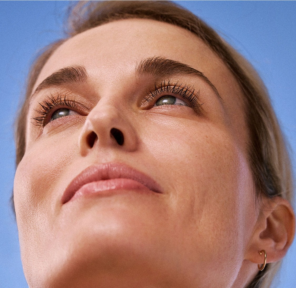 A womans face tilts upwards, looking upwards, showcasing her even, glowing skin complexion.