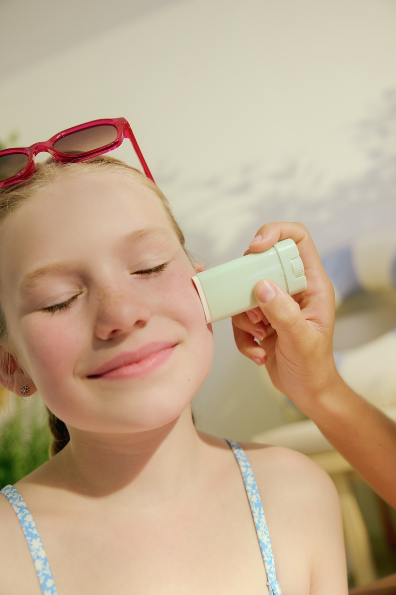 Close-up of a young girl getting face sunscreen applied with a stick
