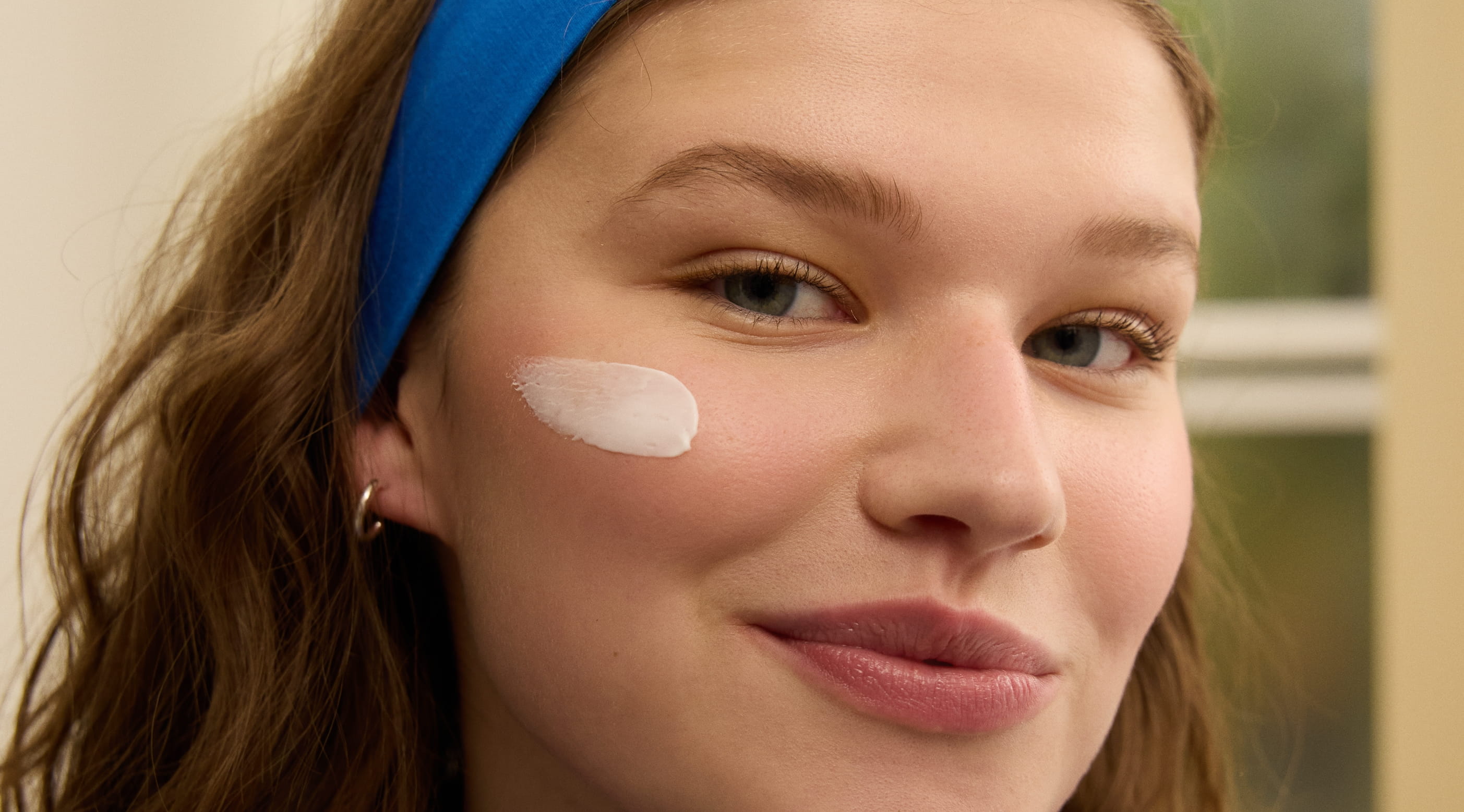 person med blått hårband, ler in i kameran och har ett streck med ansiktskräm på kinden