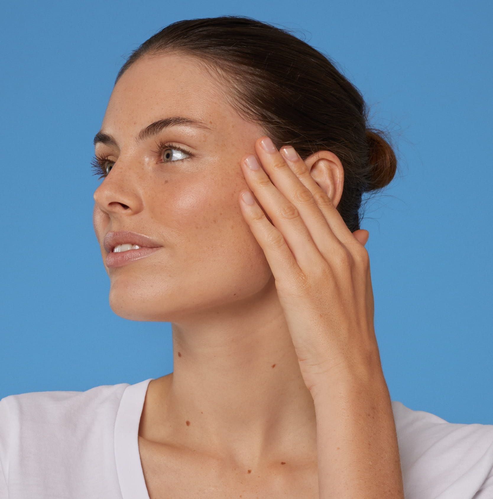 Eine Frau, die ihr Gesicht berührt und ein weißes T-Shirt trägt