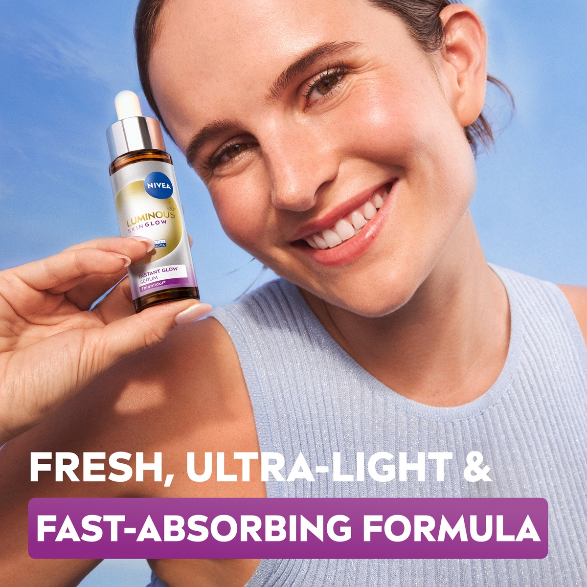 A young woman glowing complexion smiles gleefully while holding up a bottle of NIVEA LUMINOUS630® Skin Glow Liquid Refiner.