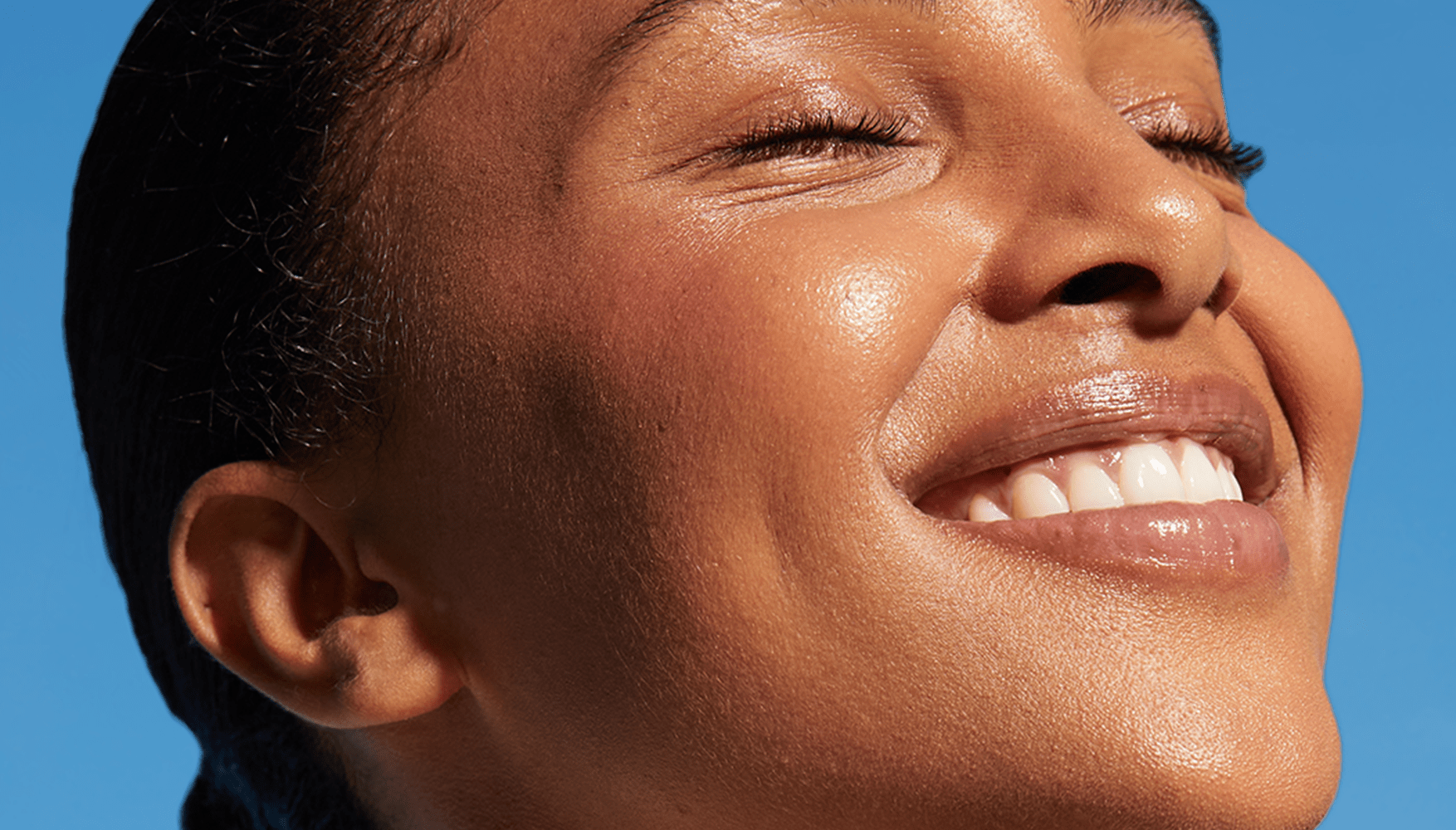 Une femme applique de la crème sur son visage, son sourire rayonne de satisfaction.
