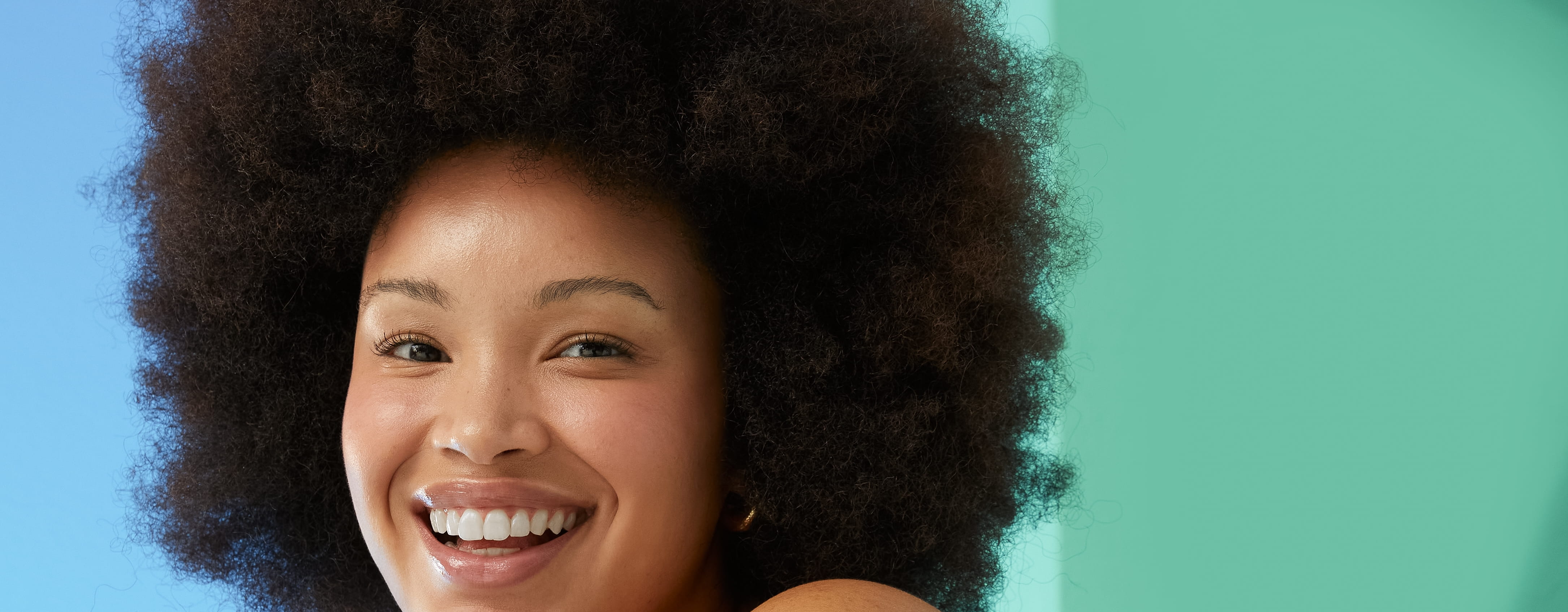 Jonge vrouw met afrohaar gebruikt Nivea Radiant and Beauty Body Lotion