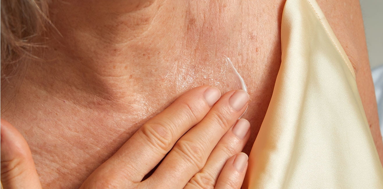 A woman's hand swipes Q10 Firming cream on her décolleté.