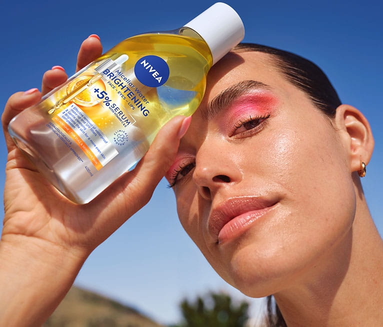 Млада жена гледа надолу и държи мицеларната вода NIVEA Brightening със серум до челото си