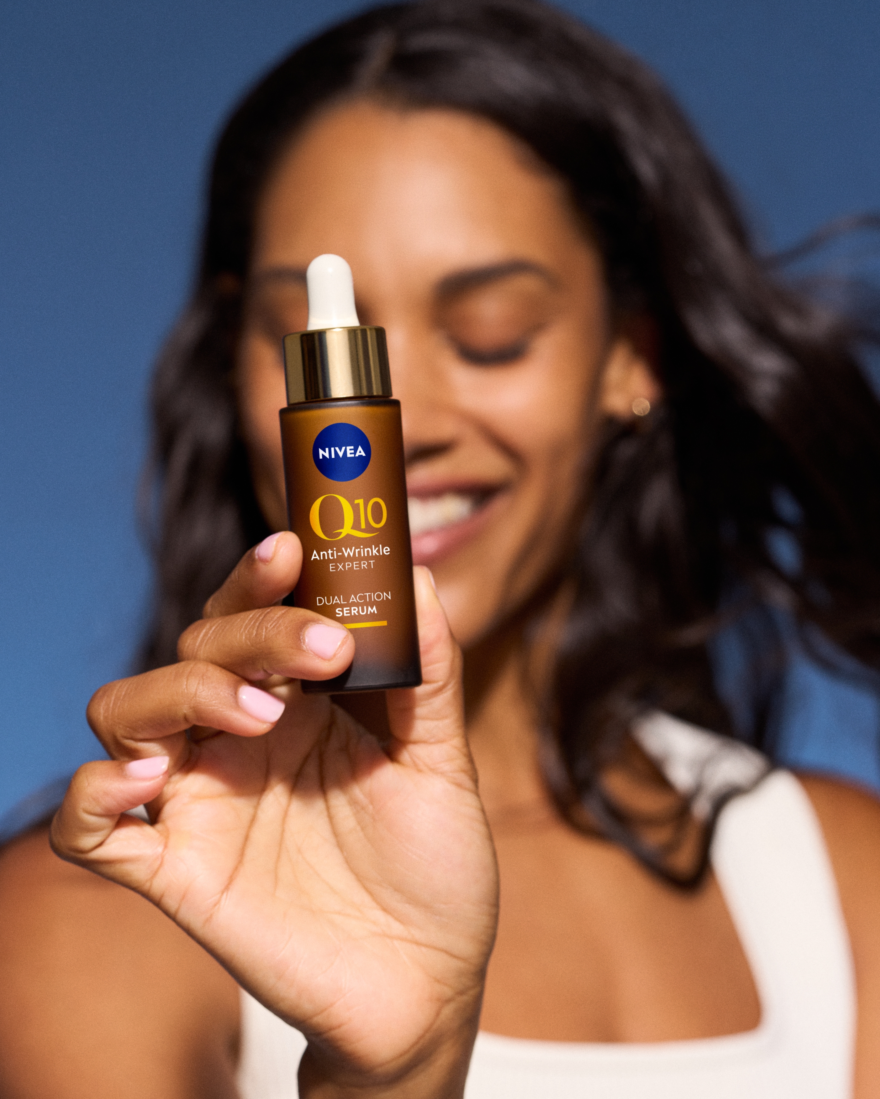 kvinna som ler och håller fram NIVEA Q10 serum framför ansiktet