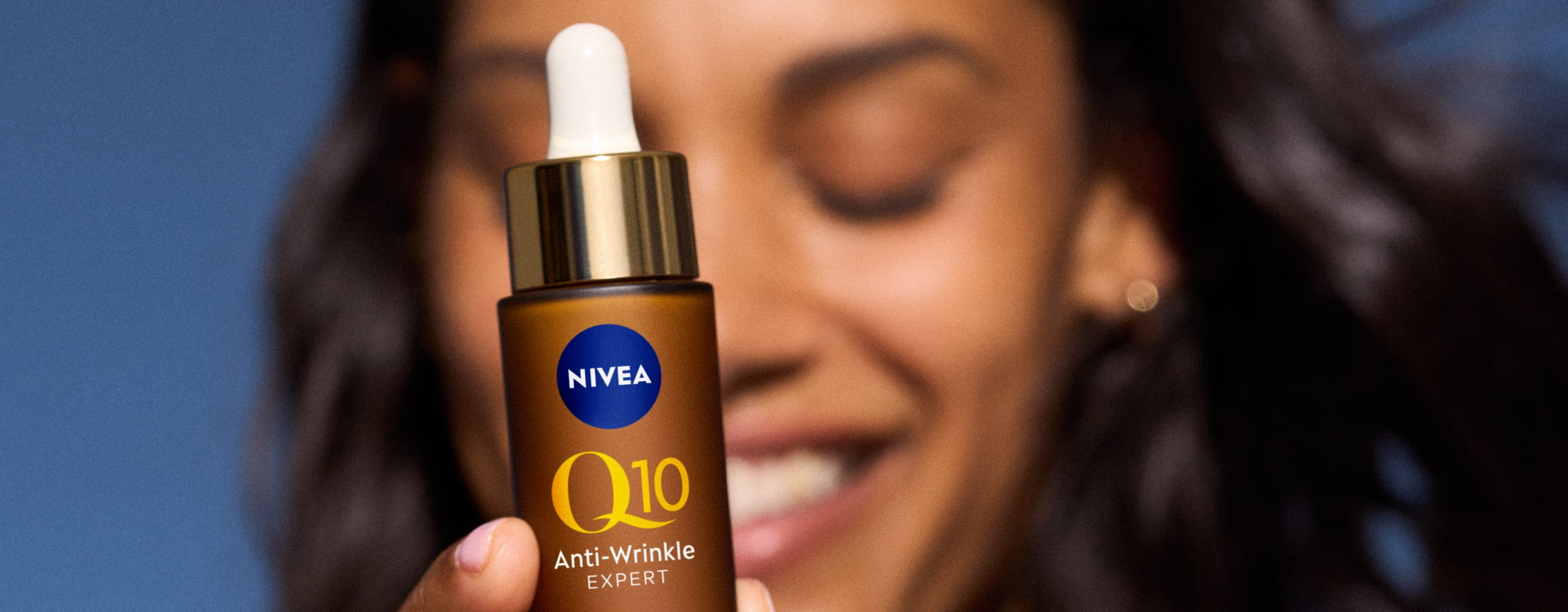 kvinna som ler och håller fram NIVEA Q10 serum framför ansiktet