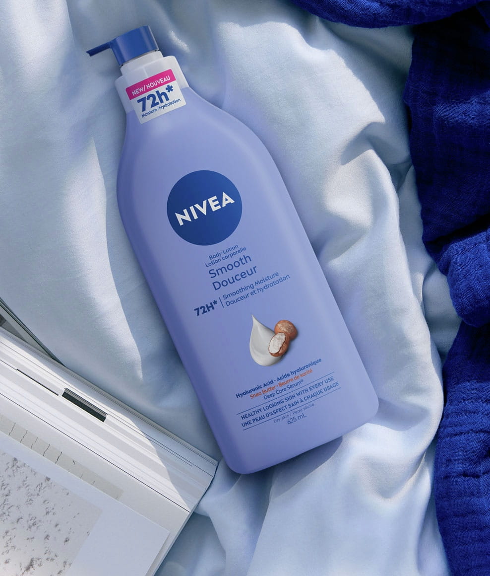 The image shows relaxing scene of a large pump bottle of NIVEA Smooth Body Lotion lying on soft, rumpled bedding.