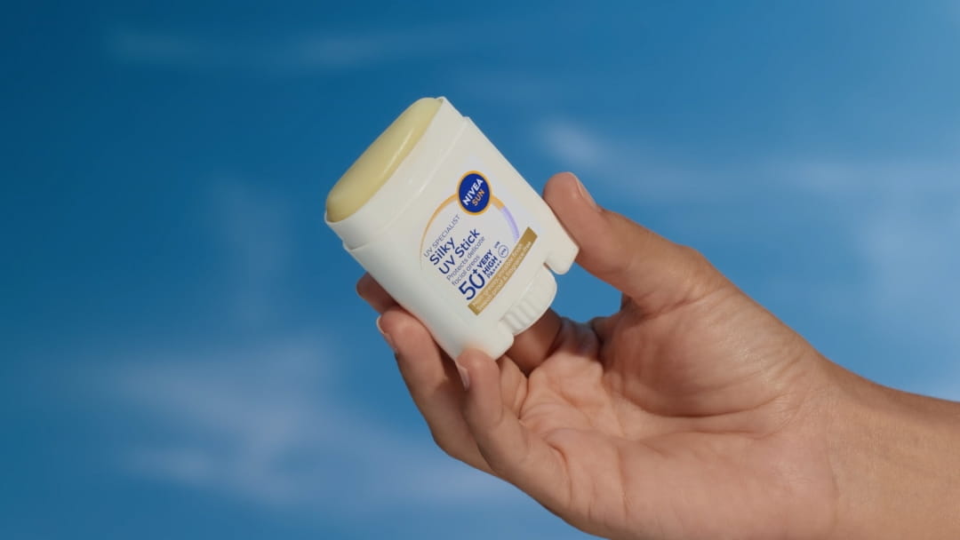 NIVEA SUN Breathable UV Specialist Silky UV Stick SPF 50+ applied to a woman's cheek; fights photoaging, no clogging.