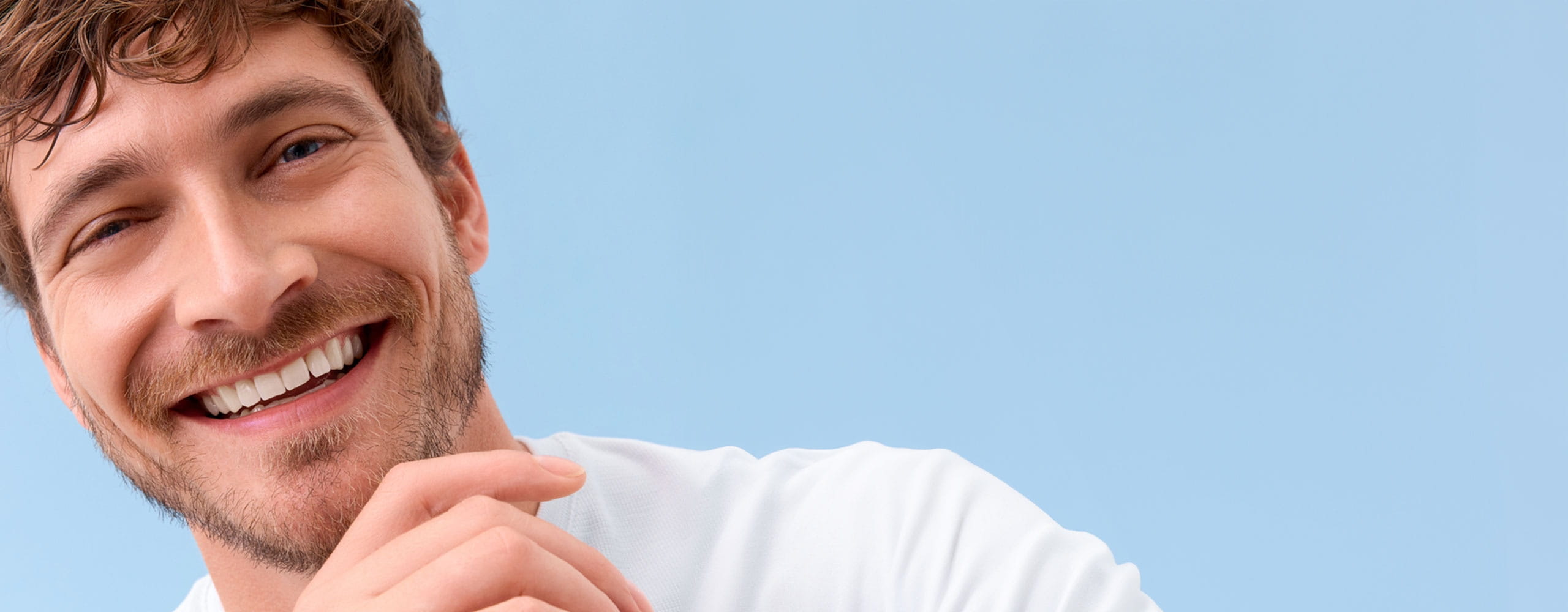 View of a person smiling while wearing a white tshirt, against a blue background.