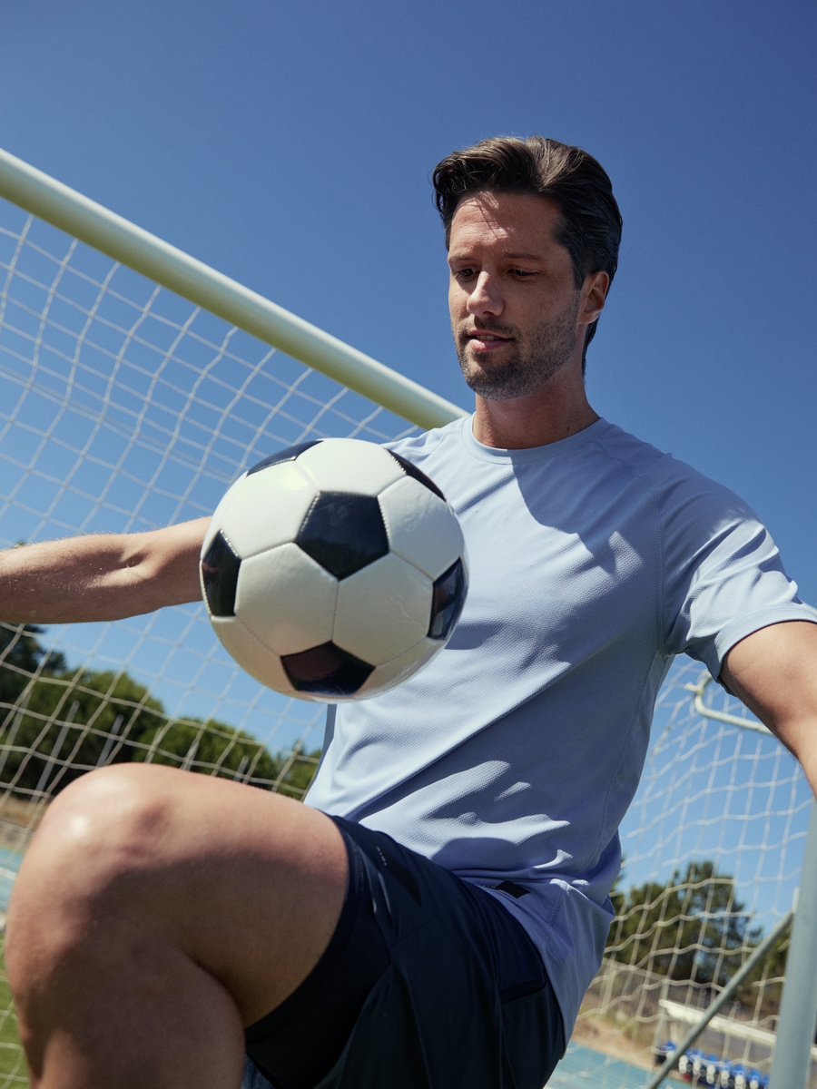 Soccer player balancing a football on his knee under the sun
