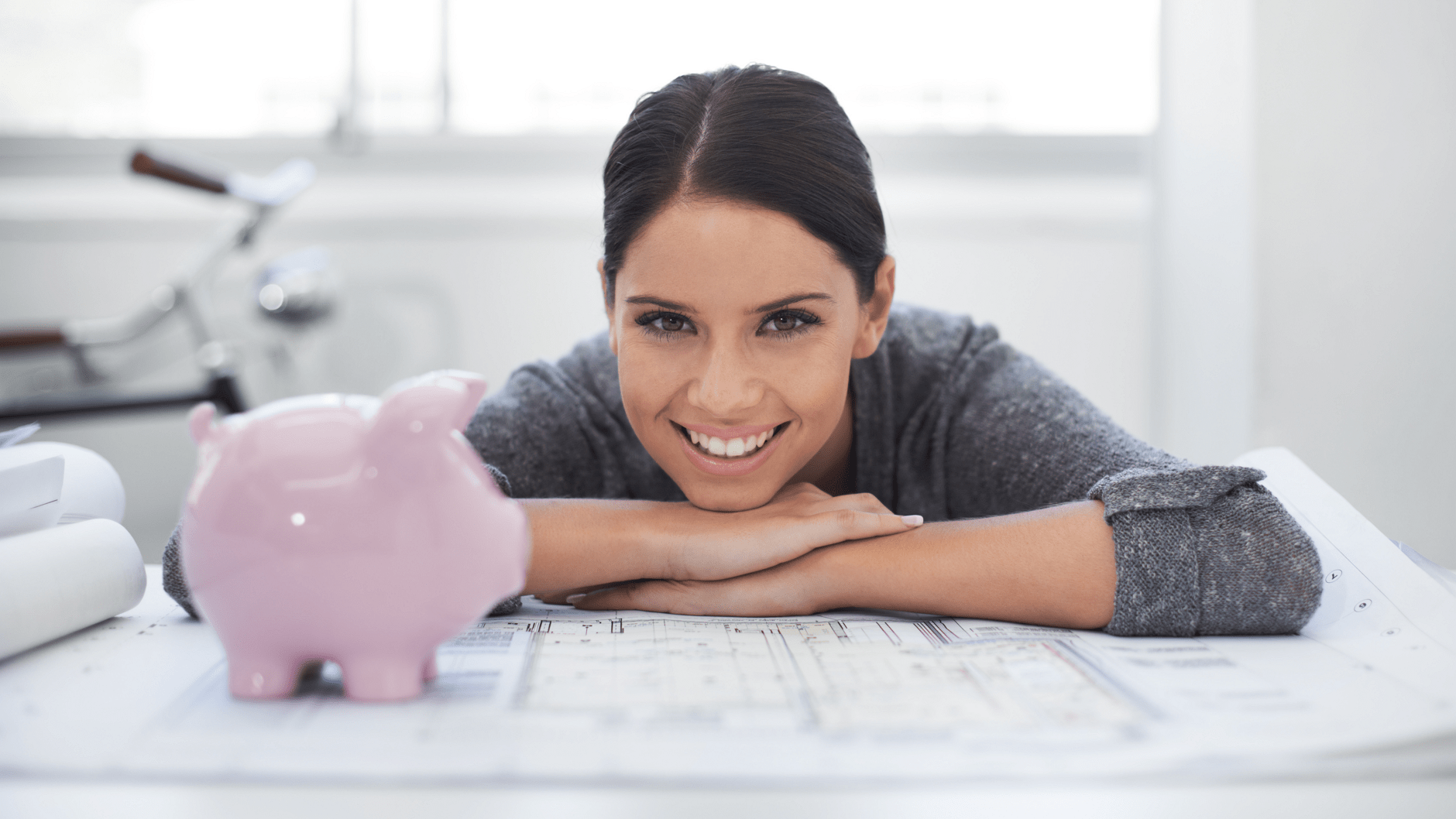 Smiling person leaning on table with pink piggy bank.