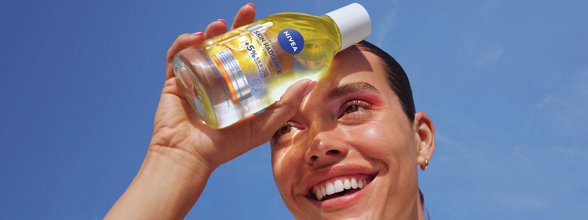 Kvinnan ler och håller NIVEA Skin Radiance Serum-Berikad Micellar Water mot pannan, som skapar skuggor.