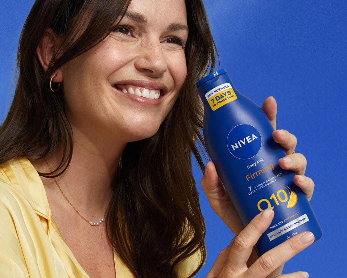 Egy nő mosolyog, kezében NIVEA Q10 feszesítő testápolóval