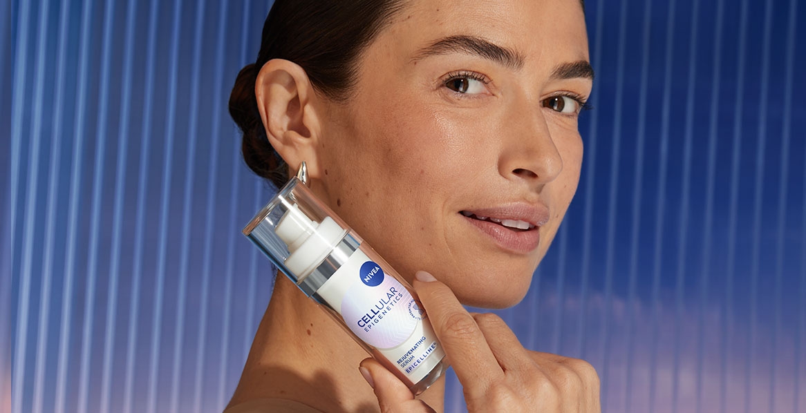 A woman smiles, holding up a bottle of NIVEA CELLULAR Epigenetics - Rejuvenating Serum with EPICELLINE®.