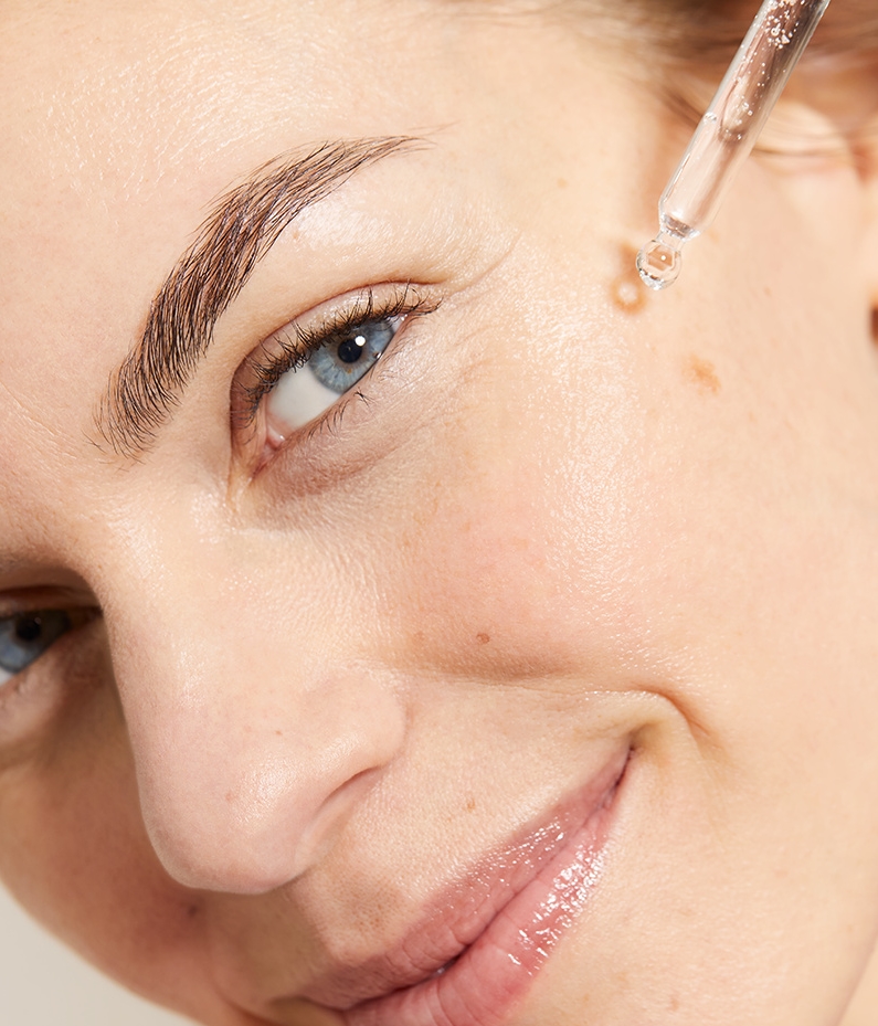 Young woman dropping Nivea serum onto her face