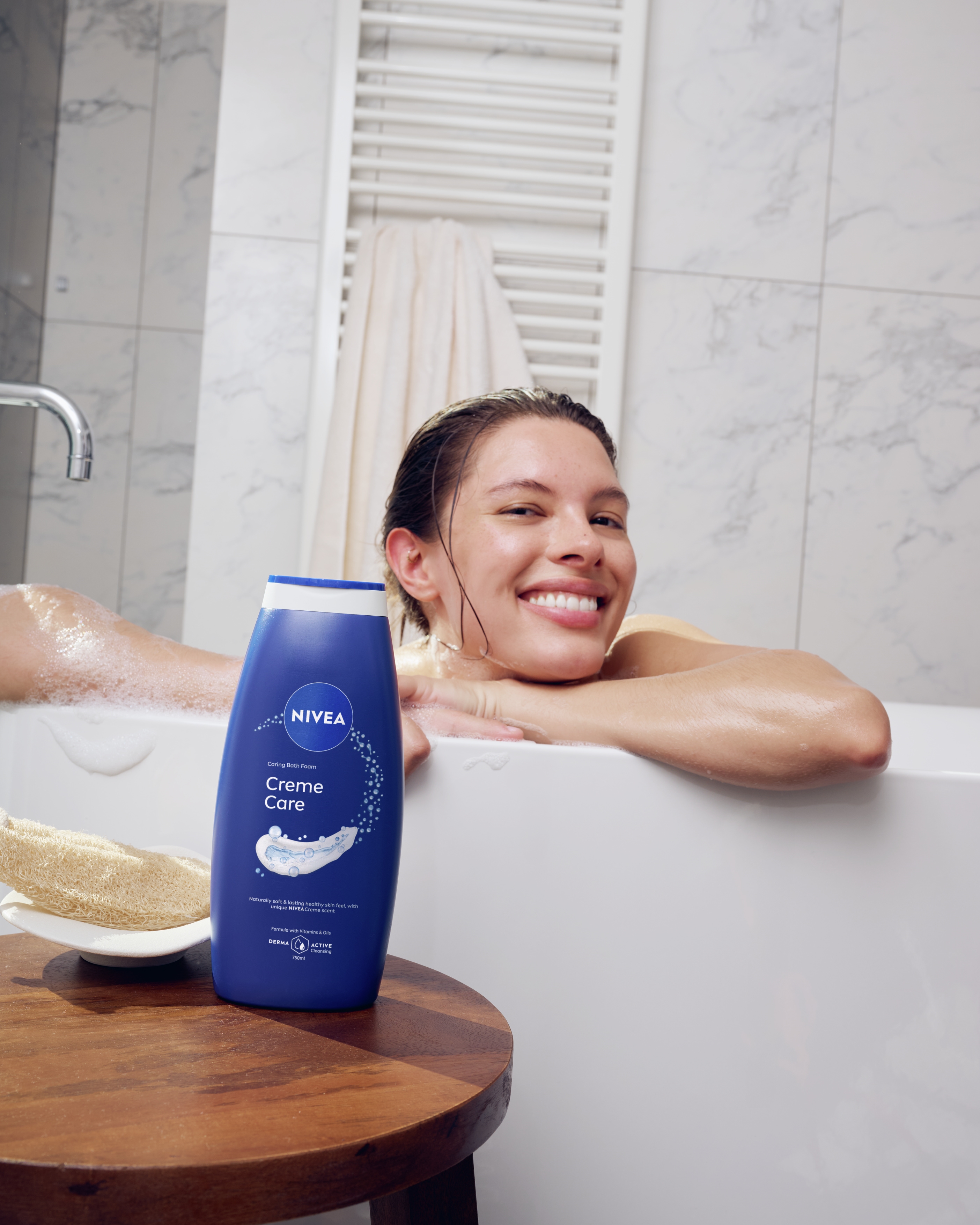 En person som badar och hänger på kanten av badkaret med armarna och ler