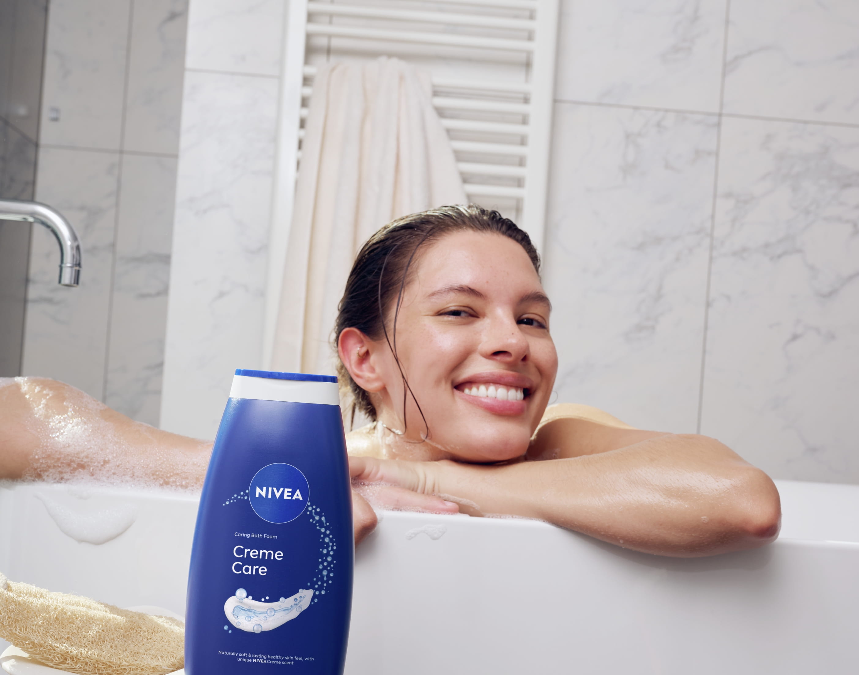 En person som badar och hänger på kanten av badkaret med armarna och ler