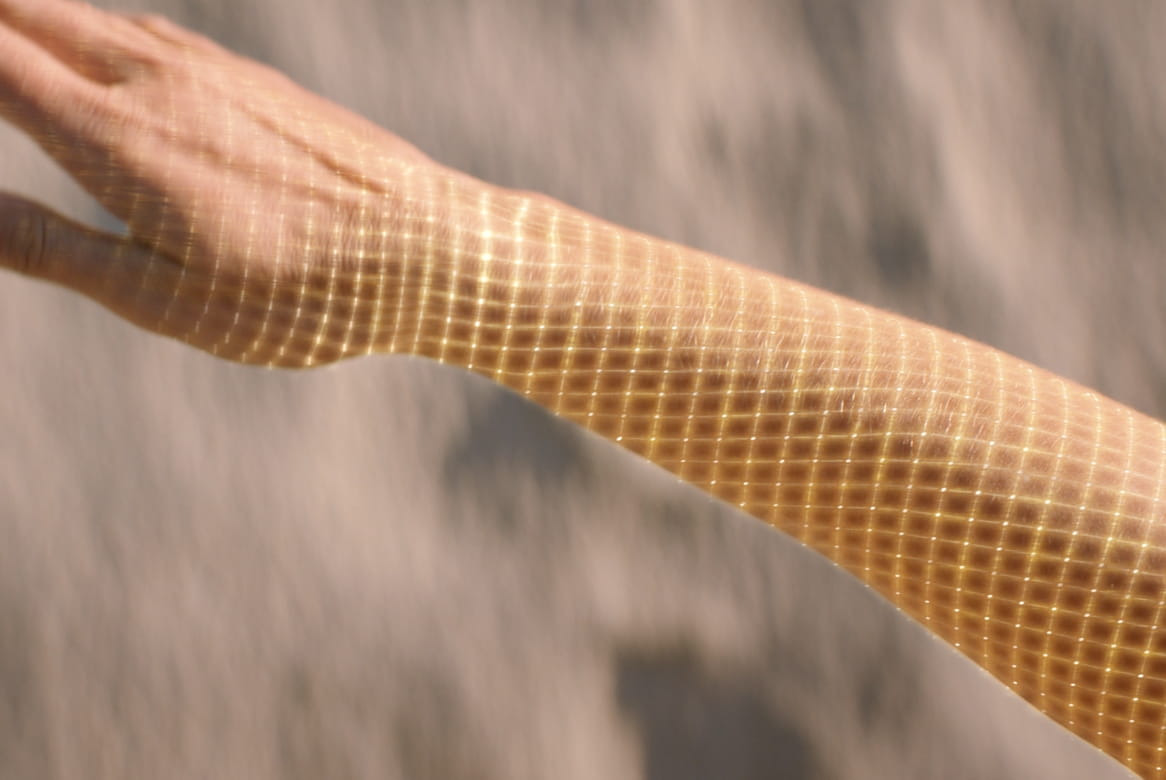 Sunlight casting a checkered shadow pattern on a person's outstretched arm.