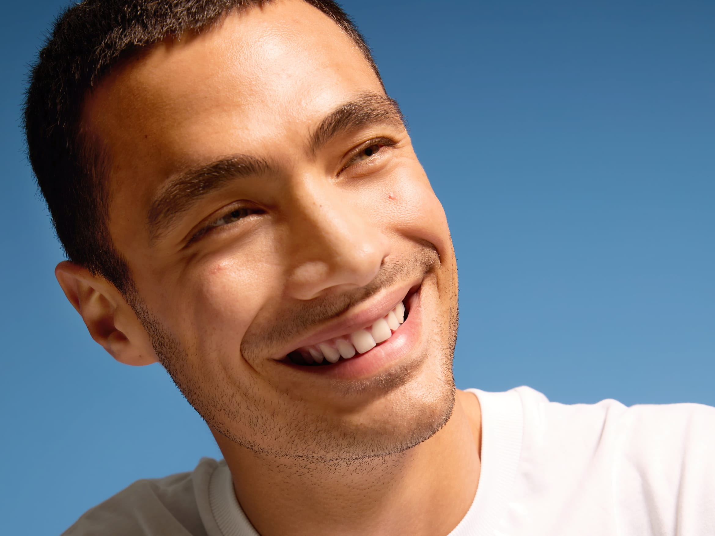 En person i vit t-shirt som ler och tittar åt höger