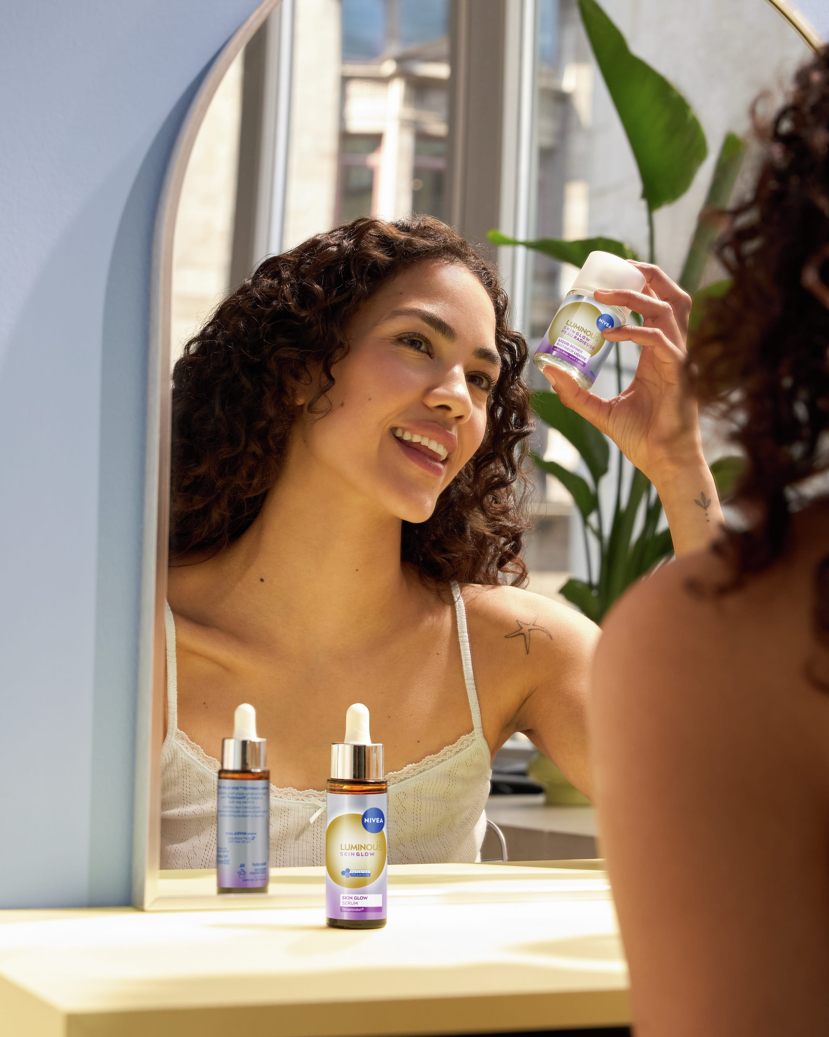 Person tittar på sig själv i spegeln, ler och håller upp NIVEA Skin Glow Daily Exfoliator