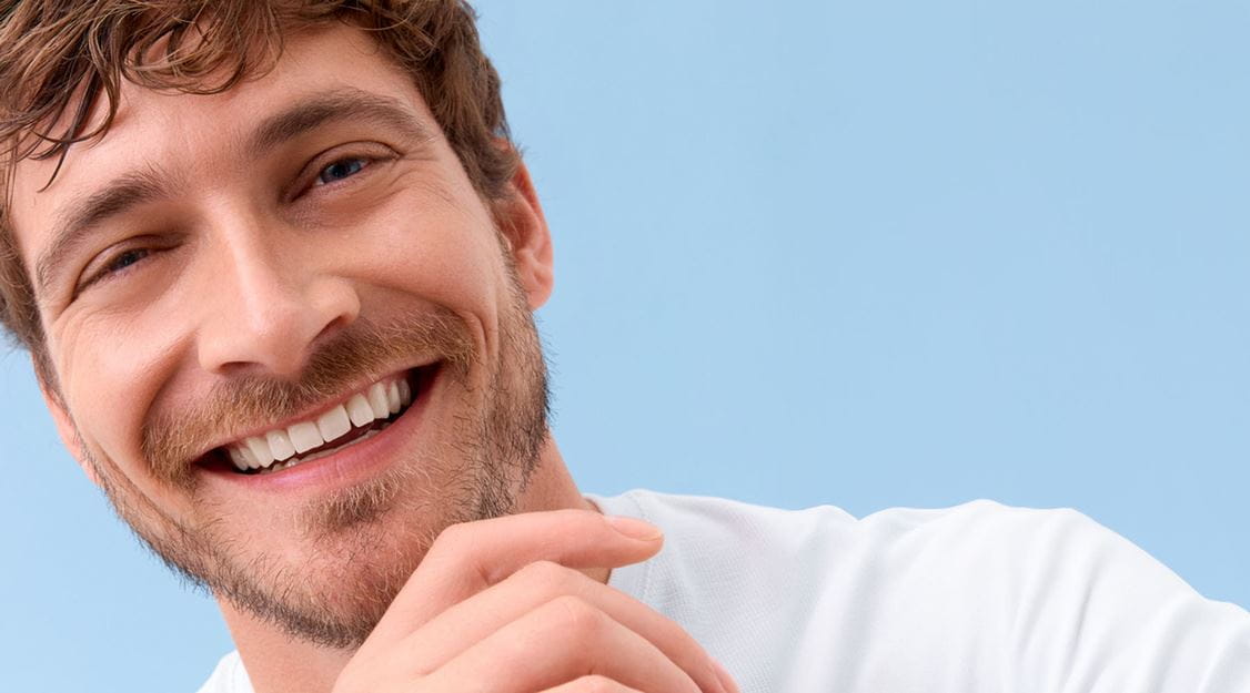 View of a person smiling while wearing a white tshirt, against a blue background.