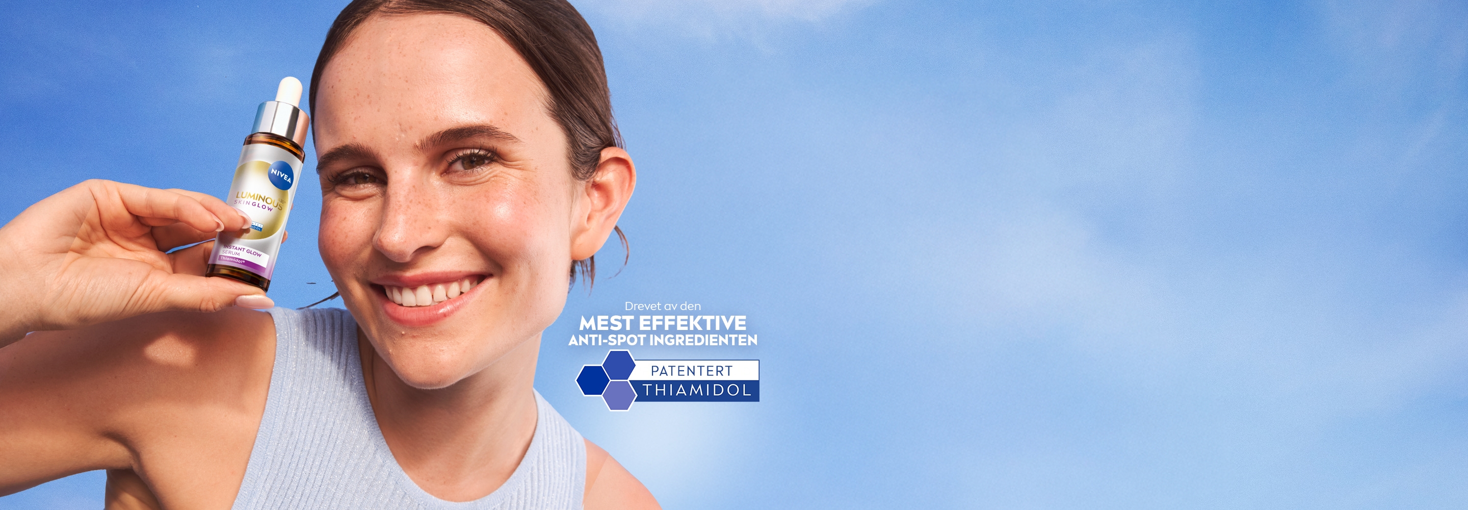 En person som smiler mens holder opp NIVEA LUMINOUS630® Skin Glow Instant Glow Serum.