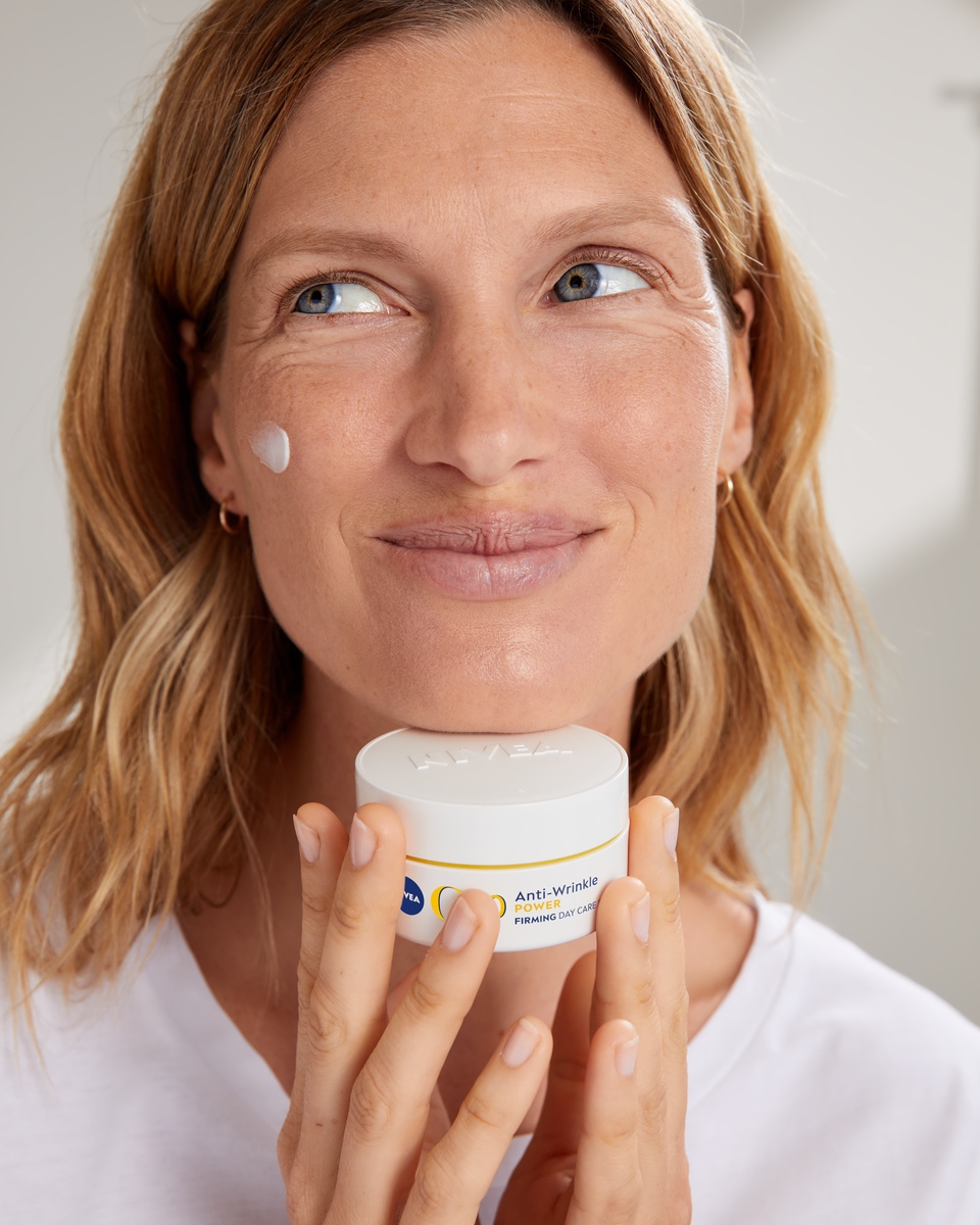 Mujer rubia usando la crema facial antiarrugas Nivea Q10.