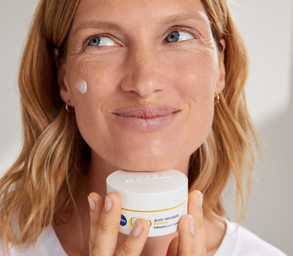 Blonde vrouw die Nivea Q10 Anti-Rimpel gezichtscrème gebruikt