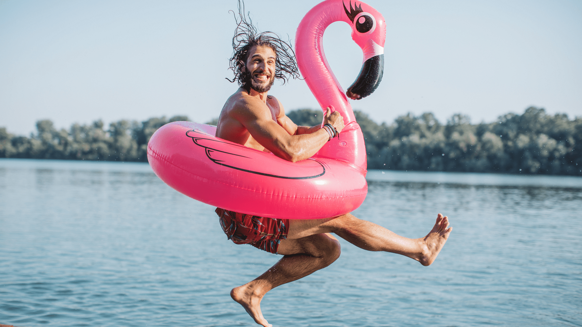 Person jumping into water with pink flamingo float.