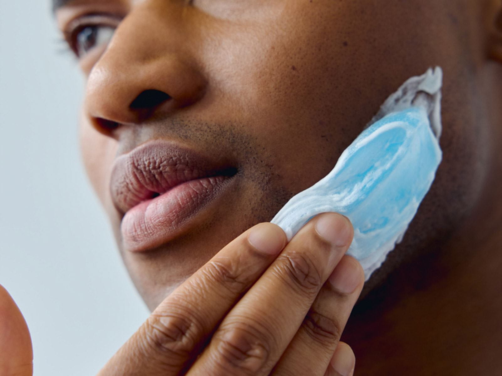 View of a person smearing a Nivea shaving gel product onto the left side of their face.