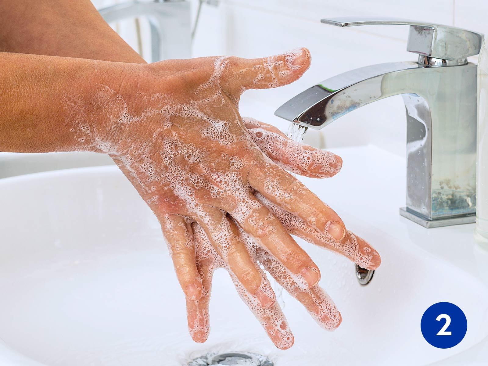 View of a person washing their hands with foaming soap in a sink.