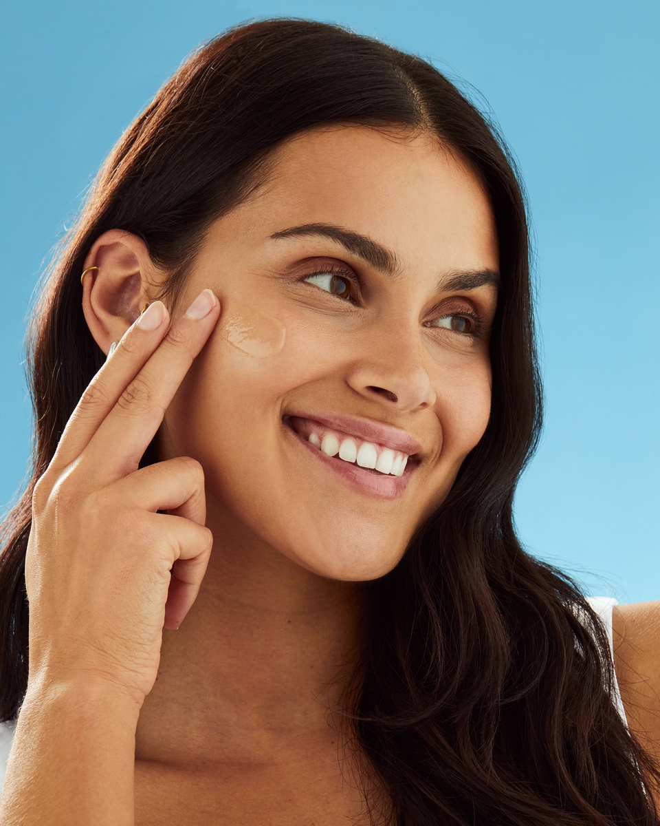 Smiling woman applying sunscreen lotion to her cheek
