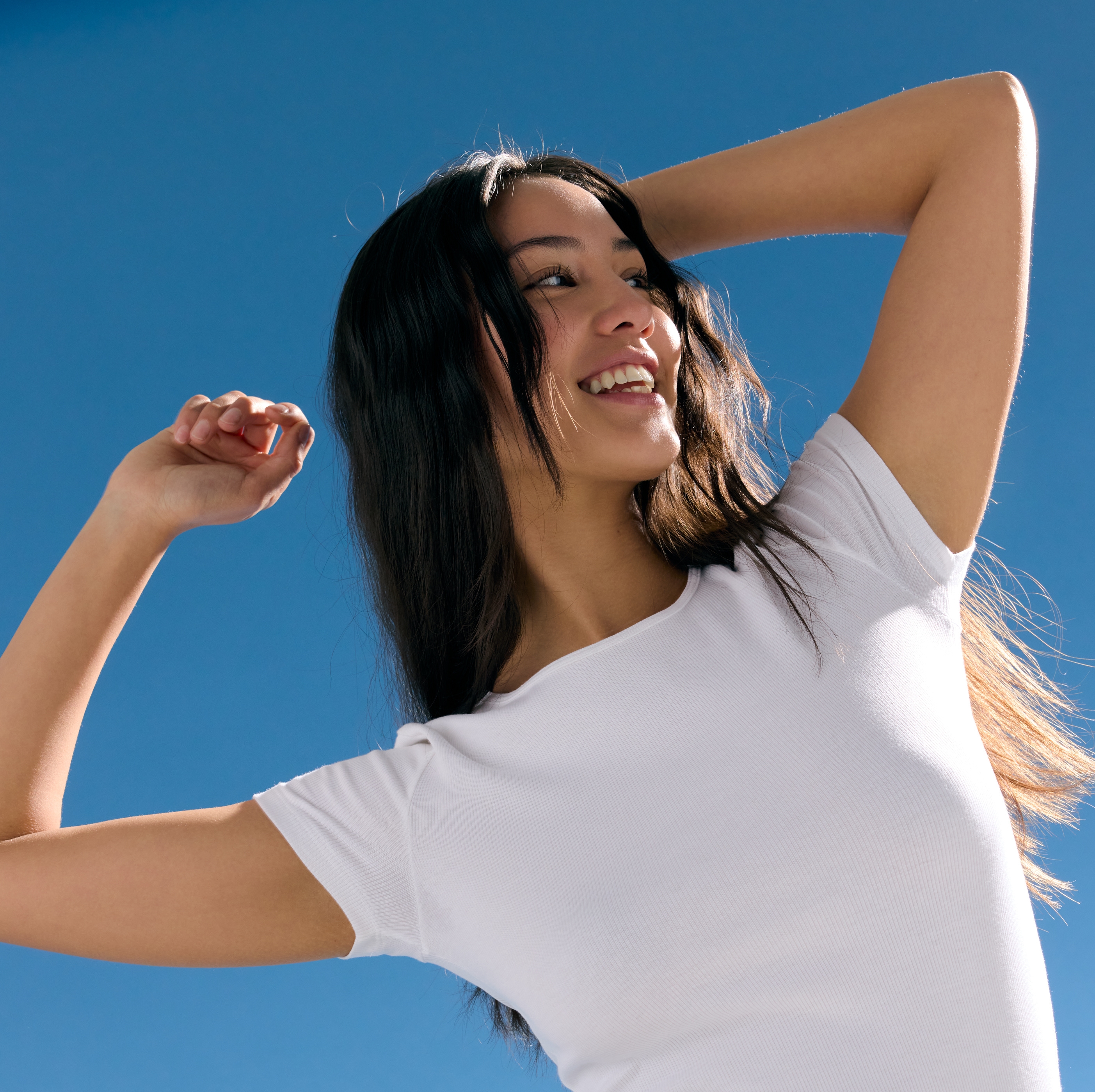 Fille portant un débardeur blanc et souriant, les mains levées