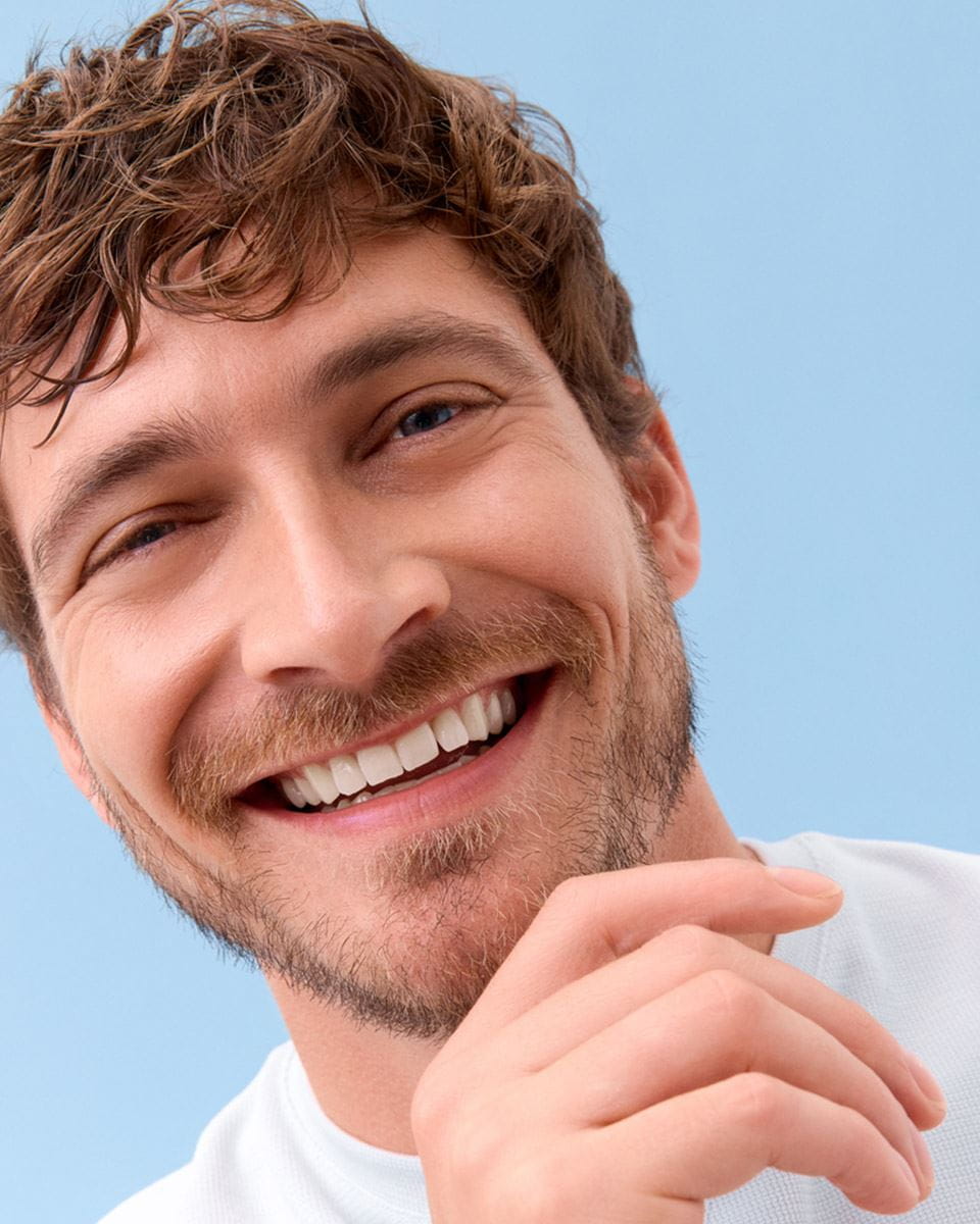 View of a person smiling while wearing a white tshirt, against a blue background.