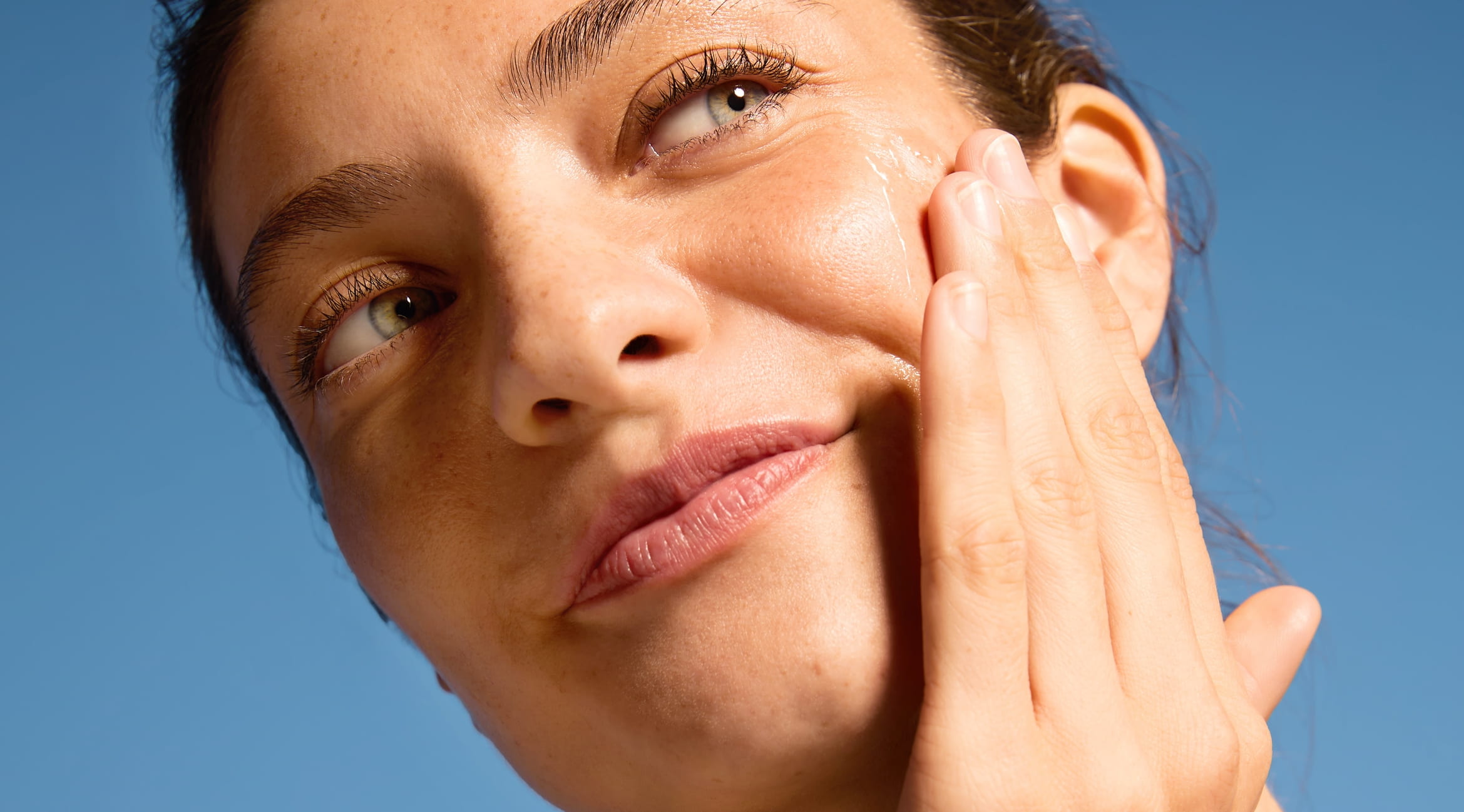 Kvinna tiltar huvudet och ler med en hand på kinden