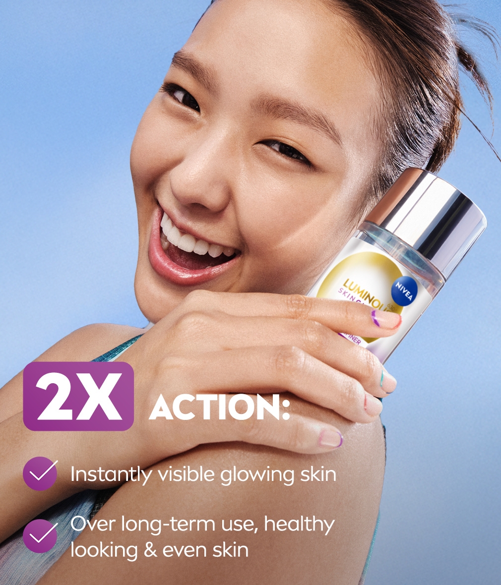 A young woman glowing complexion smiles gleefully while holding up a bottle of NIVEA LUMINOUS630® Skin Glow Liquid Refiner.