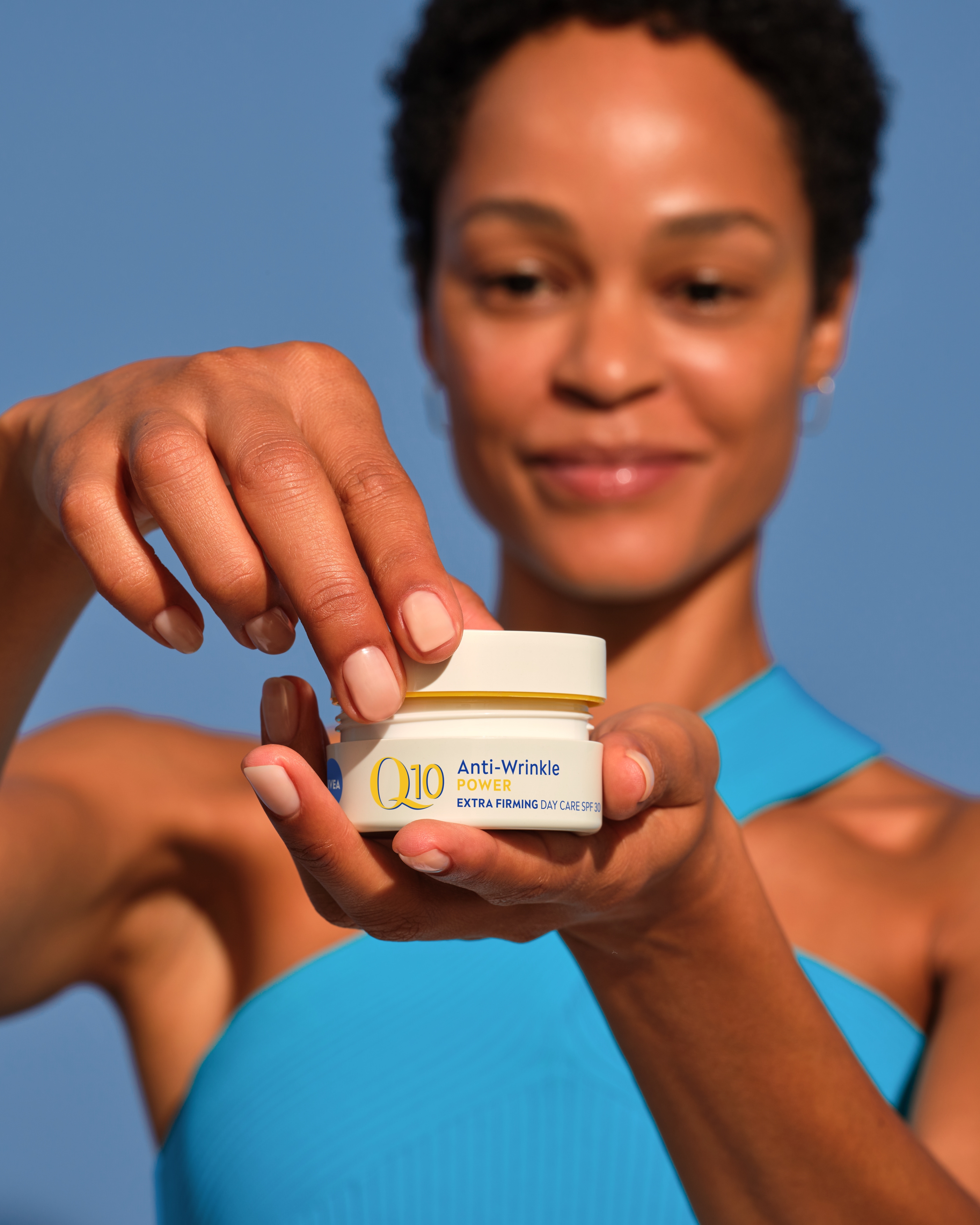 Person håller upp NIVEA Q10 Day Cream. Burken är i fokus och en hand skruvar av locket