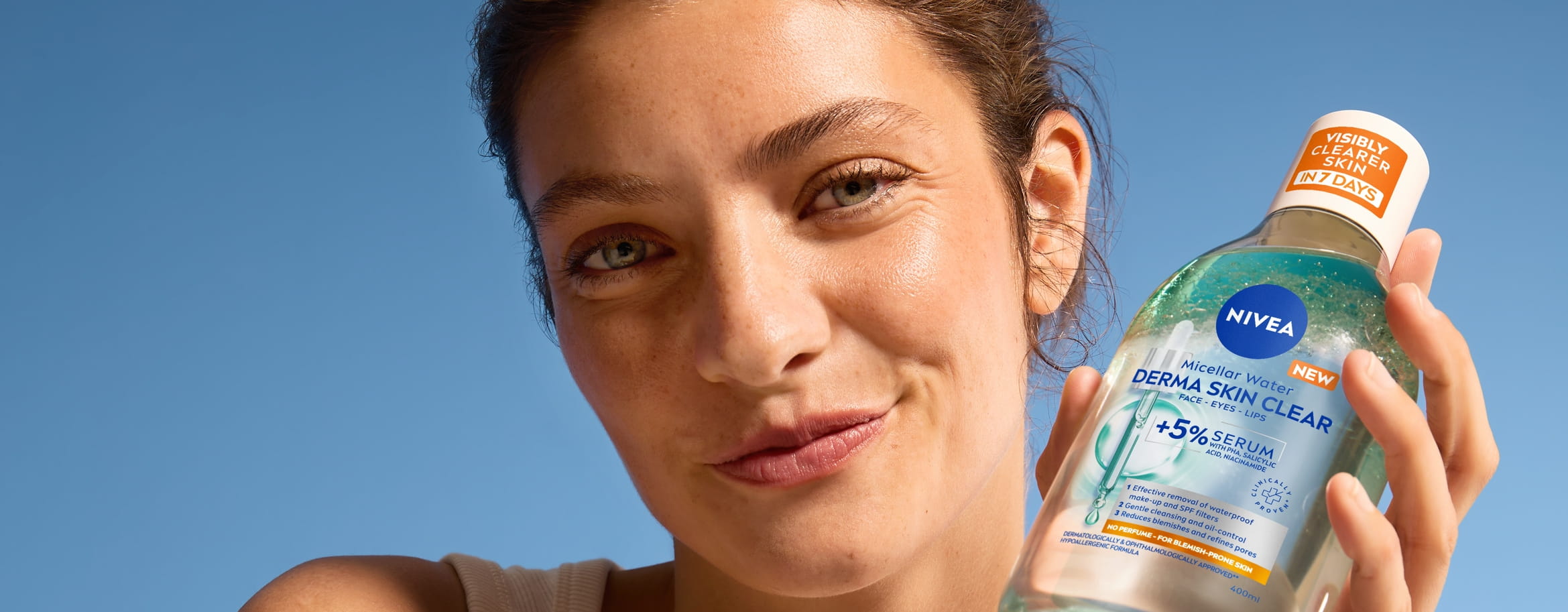 Kvinna i linne ler och håller upp NIVEA Derma control Micellarvatten