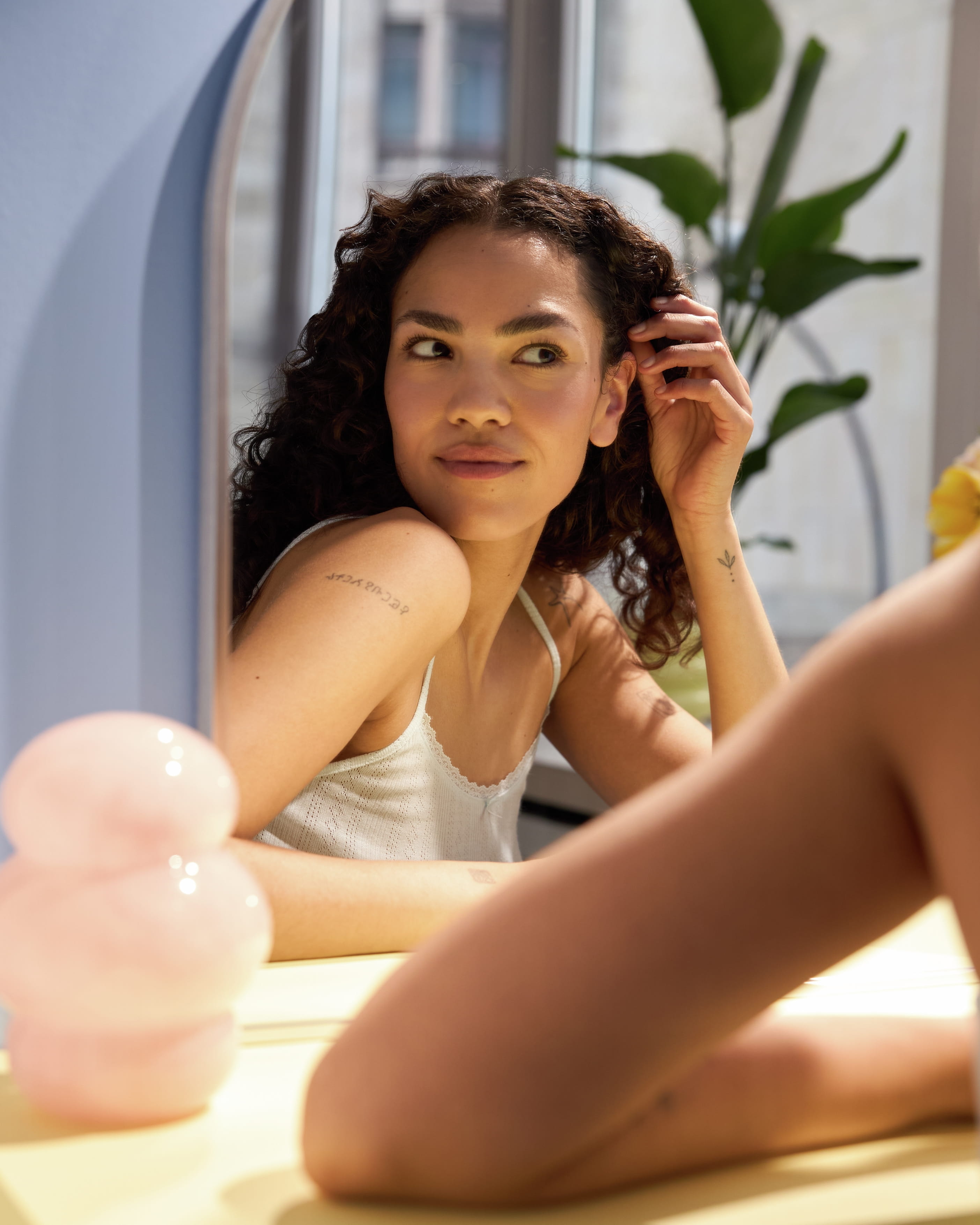 Kvinna sitter och kollar på sig själv i spegeln, tiltar ena axeln framåt och drar håret bakom örat