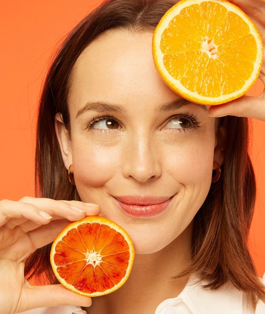 mulher segurando duas laranjas cortadas ao meio