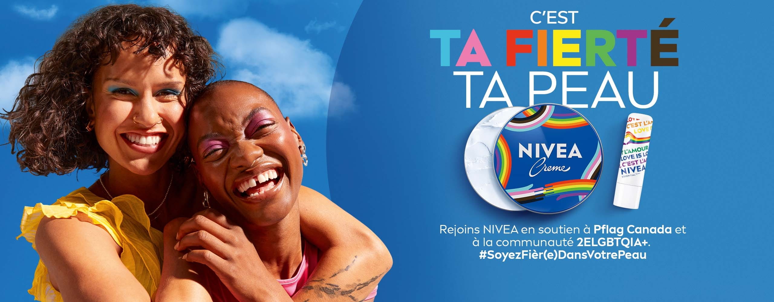 Deux personnes souriantes s'entrelaçent sur fond de ciel bleu, avec Pot NIVEA CREME Fierté série limitée et baume à lèvres NIVEA Essential Fierté série limitée, pour promouvoir la campagne « Soyez fièr(e) dans votre peau » en soutien à la communauté 2SLGBTQIA+.